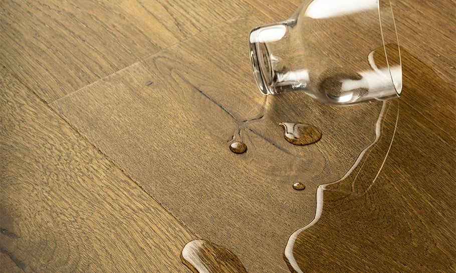 brunt trägolv med utspillt vattenglas